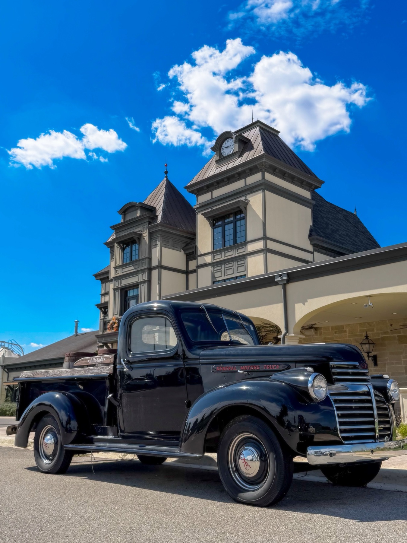 A black 1940s GMC pickup parked in front of the Altstadt Brewery clock tower under a deep blue sky