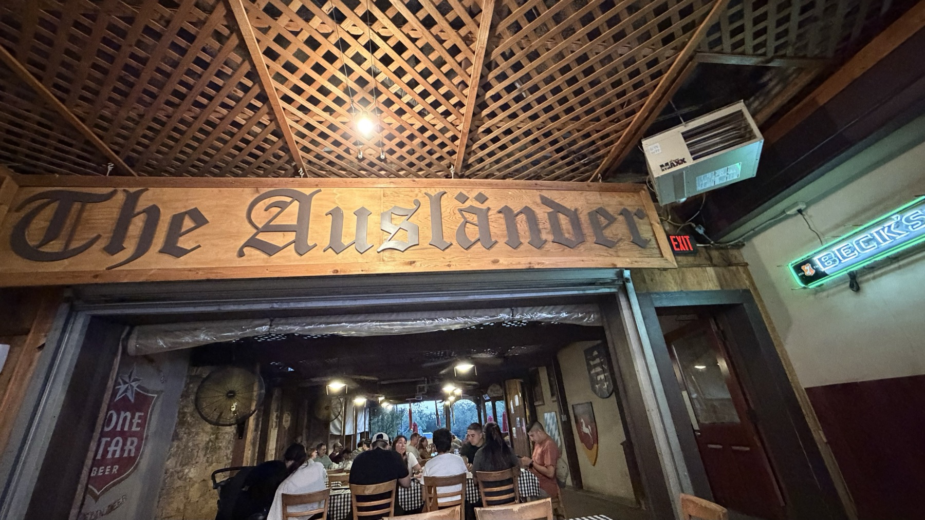 The carved Gothic-lettering Ausländer sign over the entrance to the open lattice-roofed dining hall, neon Beck's sign to the right