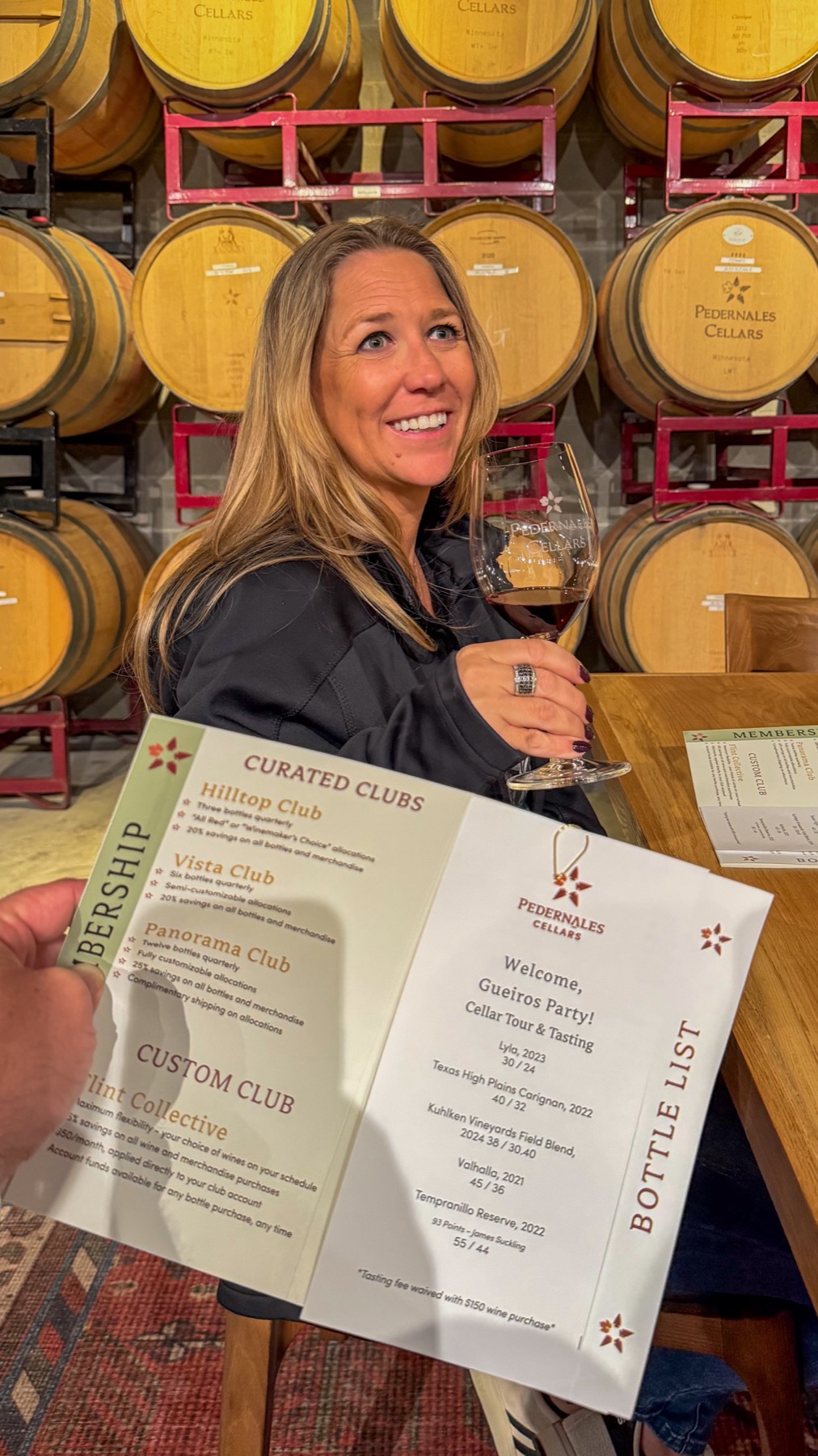 Kim holding the printed bottle list and a tasting glass in front of the barrel wall