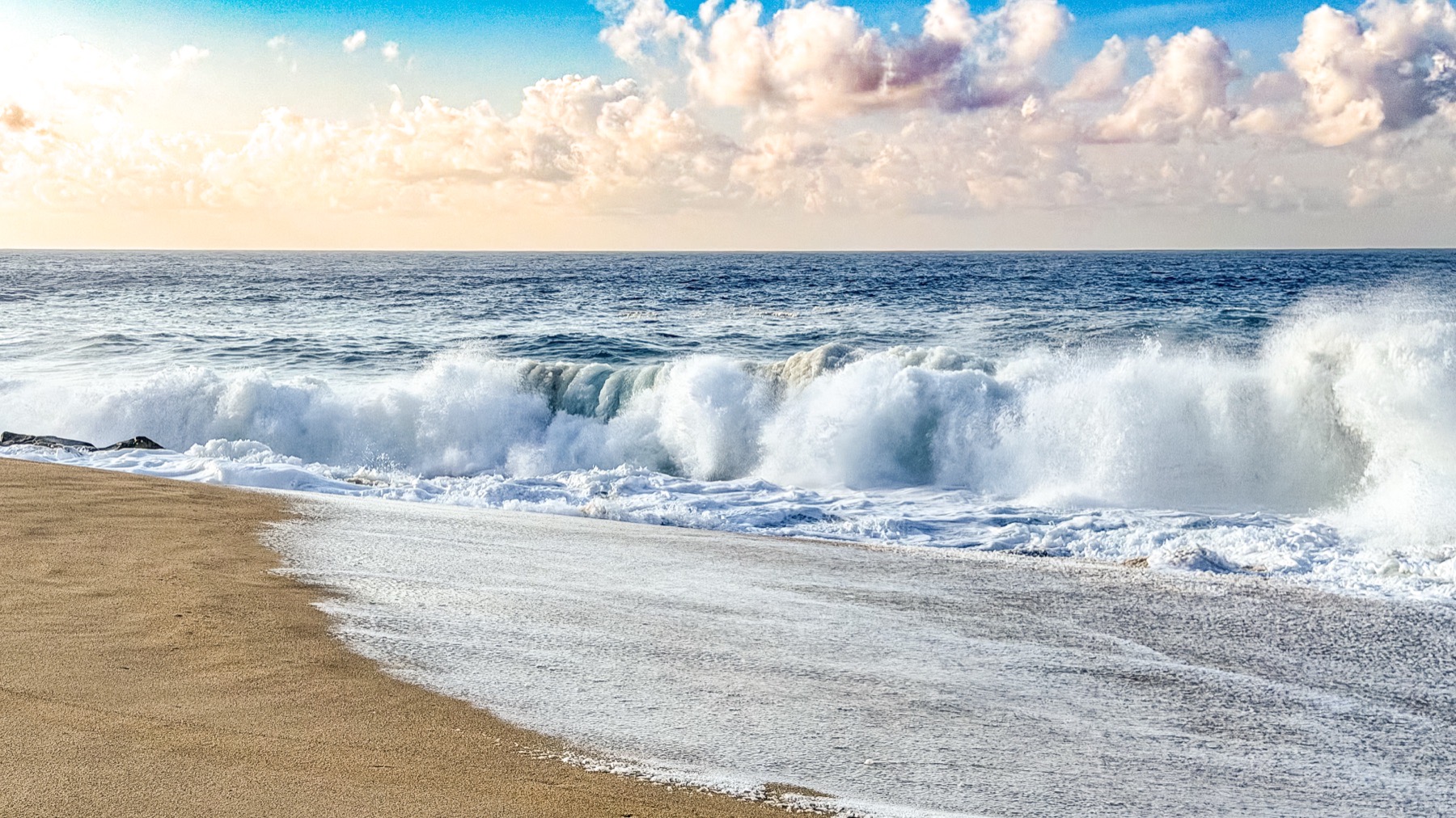 Heavy surf breaking onto the beach under a bright sky