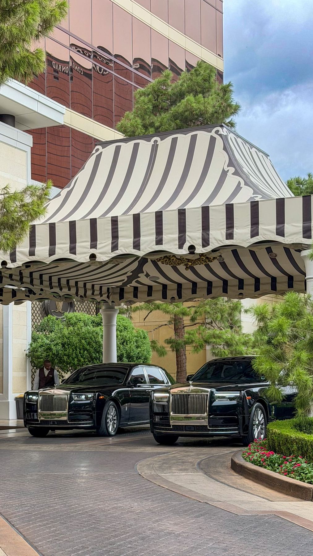 Two black Rolls-Royce Phantoms parked under a striped porte-cochère