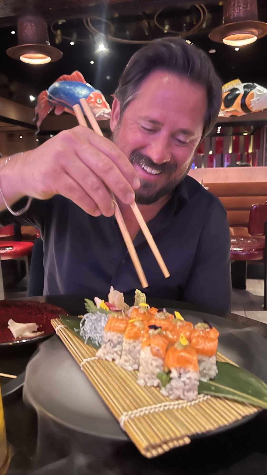 Matt reaching for a salmon roll with chopsticks at a sushi counter